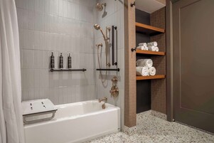 A modern bathroom with a white bathtub, a shower with gold fixtures, and shelves with towels.
