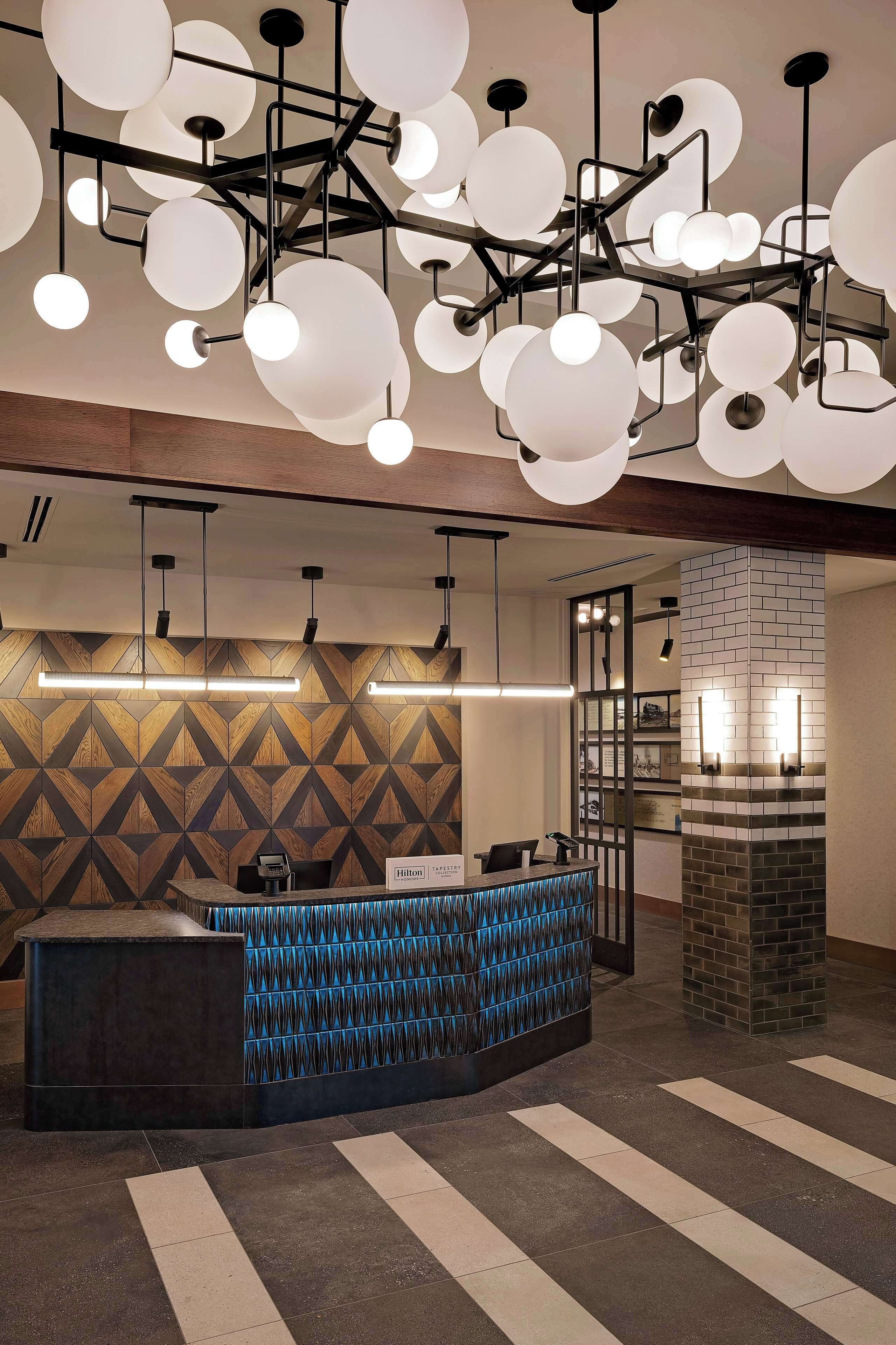 Zona de recepción de hotel con diseño moderno, que incluye un mostrador de recepción, pared con patrón geométrico e iluminación contemporánea.
