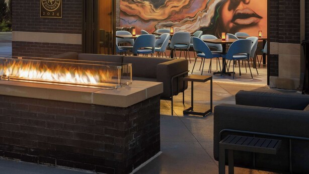 An outdoor seating area with a fire feature and a mural. - Hotel Nickel Plate Fishers, Tapestry Collection By Hilton (Fishers)