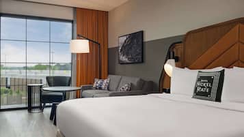 A hotel room with a large bed, a sofa, a small table, and a chair. There is a window with a view of the outside.