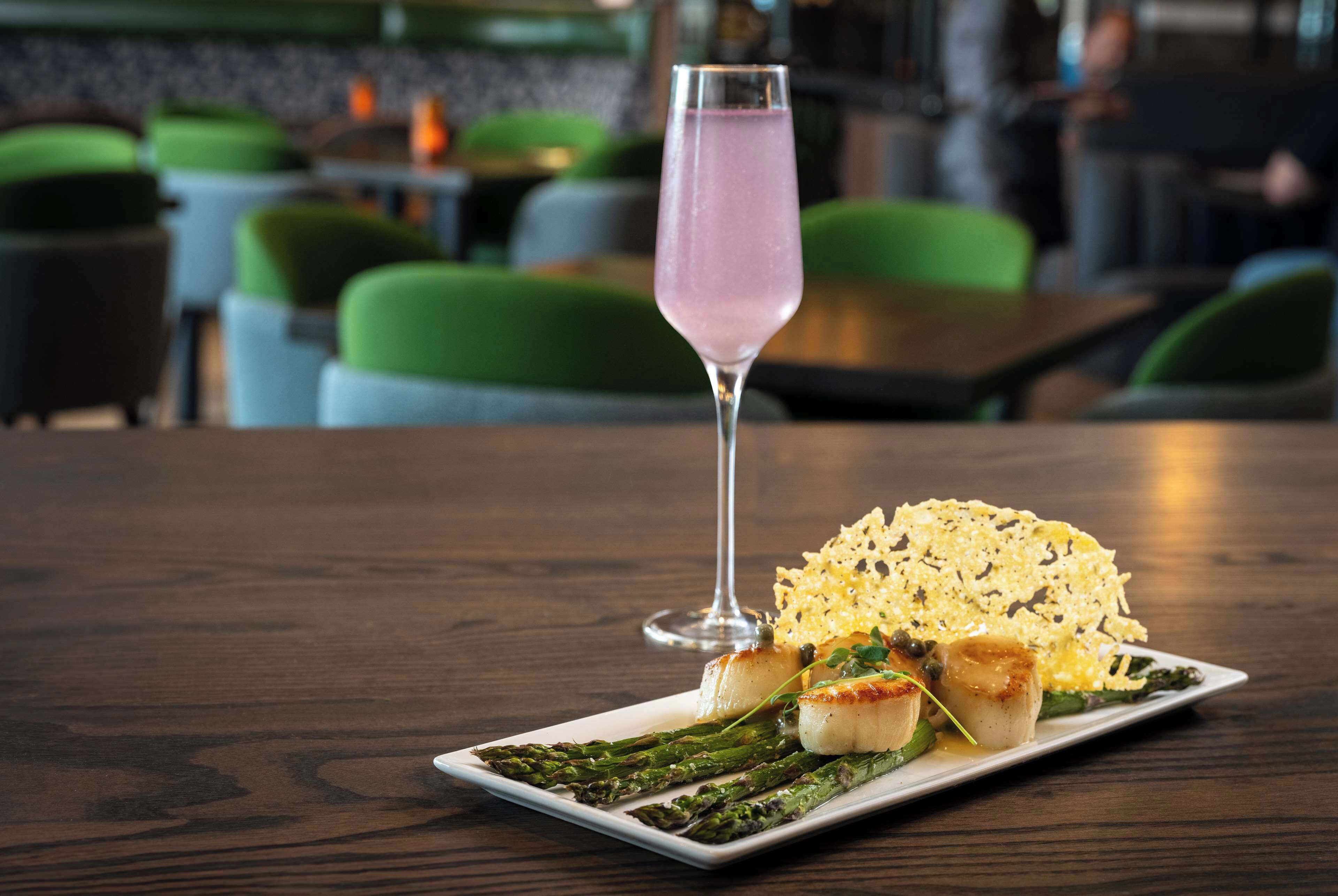 A dining table with a plate of food, a glass of pink drink, and a green chair in the background.
