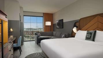A hotel room with a large bed, a sofa, a desk, and a chair. There is a window with a view of buildings.