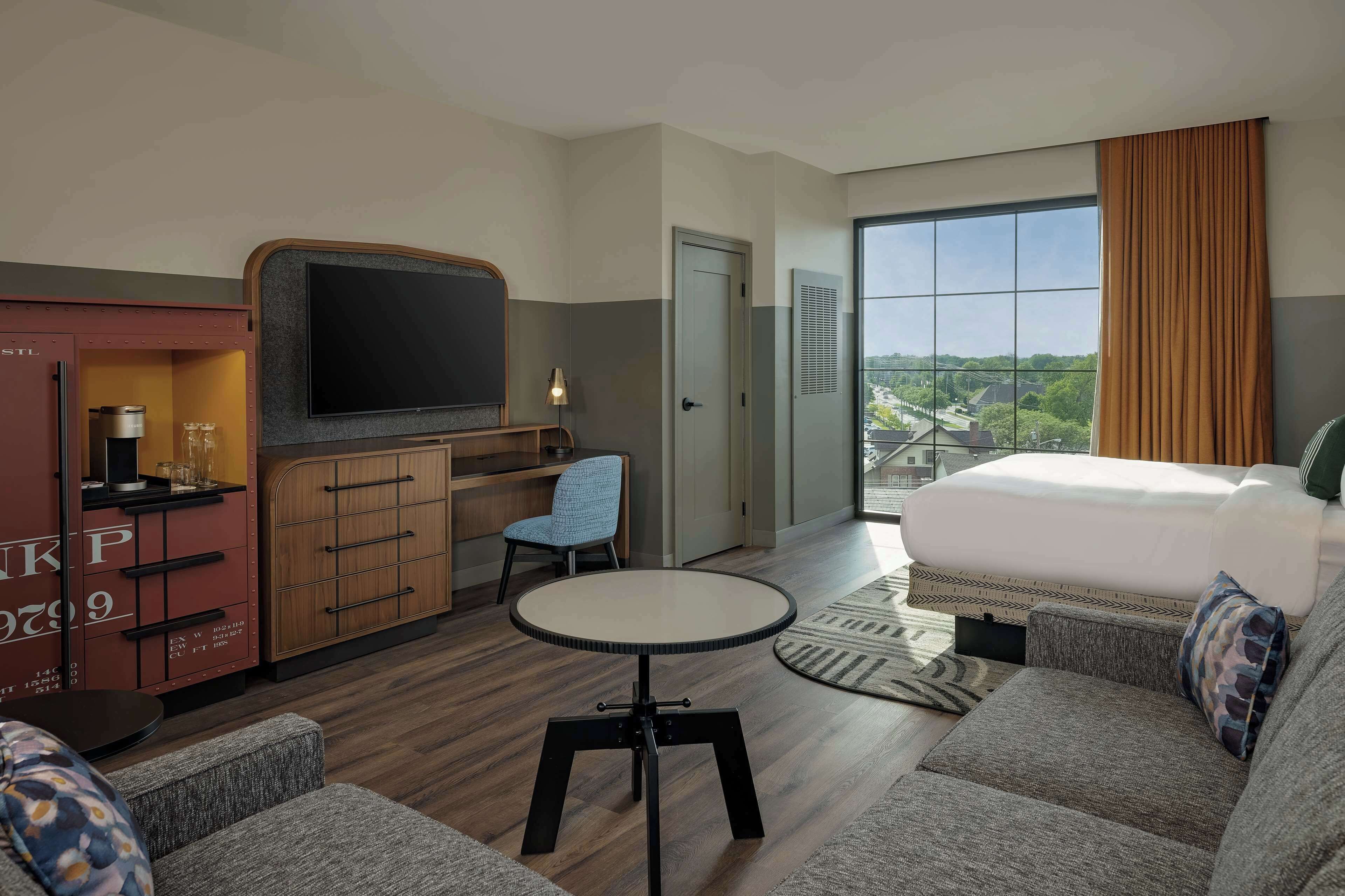 Une chambre d’hôtel avec un lit, un bureau avec une télévision, une chaise et une petite table.