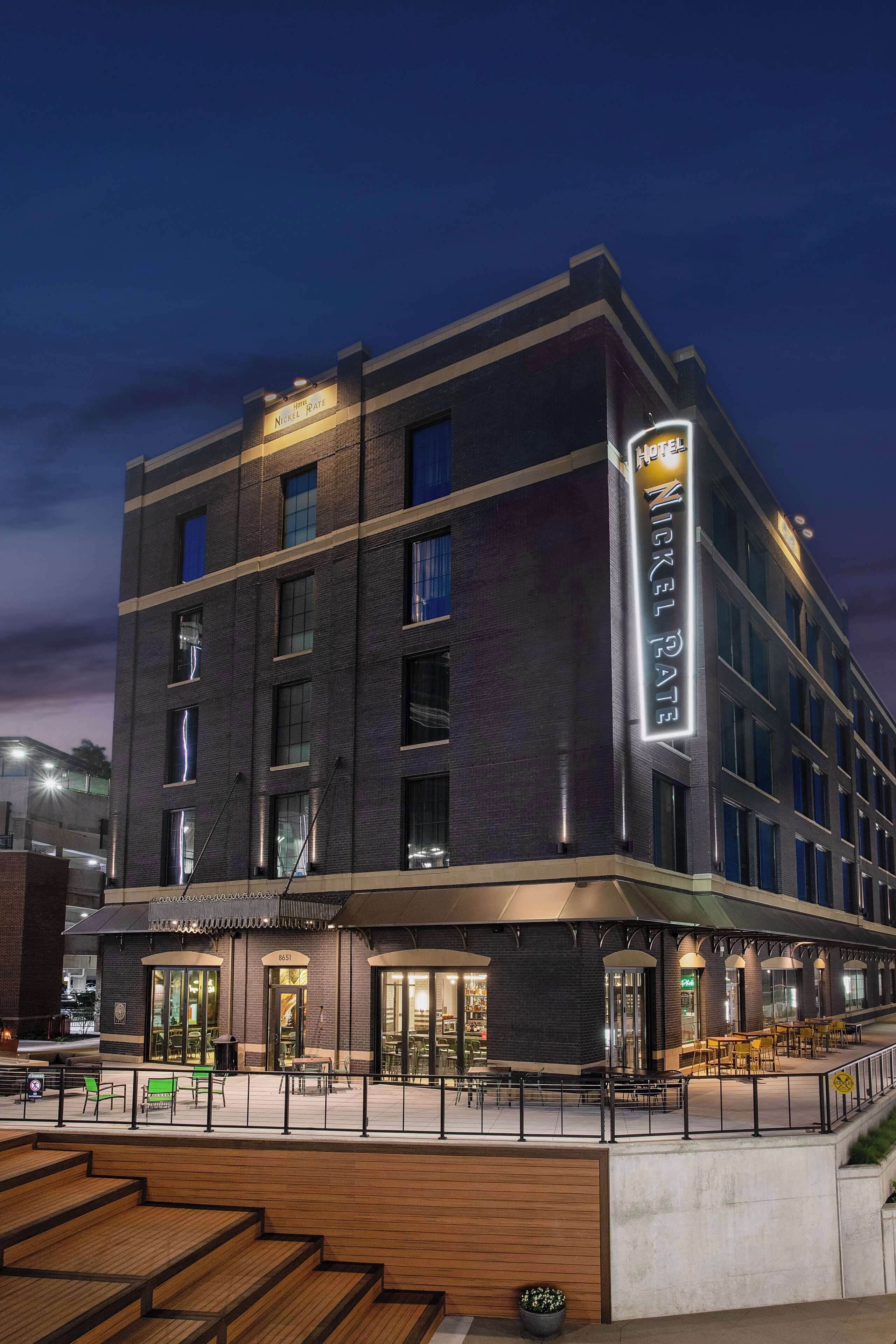 Um hotel com vários andares e um letreiro chamativo com a inscrição "Nickel Plate", área de estar externa e escadaria que leva à entrada.