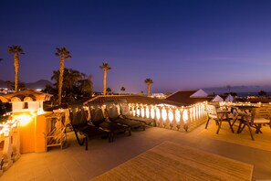 Relax in style with comfortable lounge chairs and tables, surrounded by a decorative wall and lush palm trees.