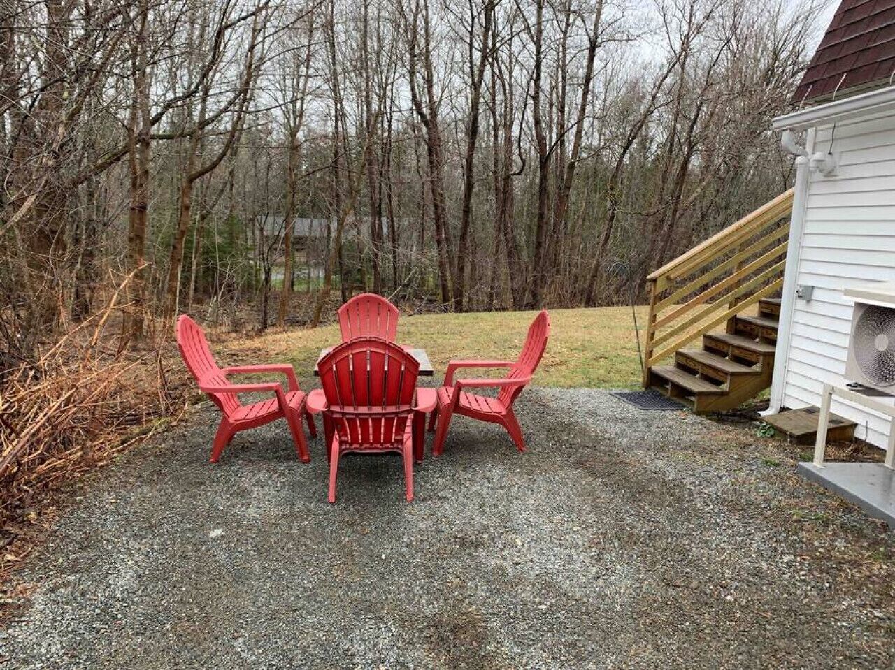 Un patio de grava con cuatro sillas Adirondack rojas y una mesa.