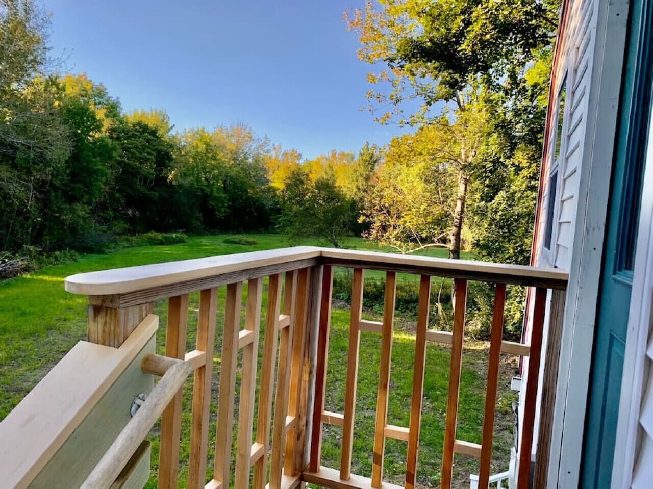 A wooden deck with a railing overlooking a grassy yard and trees.