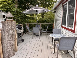 Una terraza de madera con una parrilla, sillas, una mesa y un paraguas a rayas.