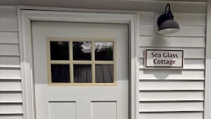 A white door with a window, a sign reading 'Sea Glass Cottage,' a doormat, and a lamp post.