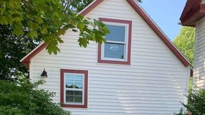 A two-story house with a red-framed window and a small garden area with a metal fence. - Sea Glass Cottage- New, Peaceful, Path to Beach (Bar Harbor)