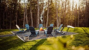 A fire pit surrounded by Adirondack chairs in a forested area.