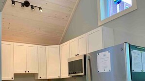 A kitchen with white cabinets, a stainless steel refrigerator, a microwave, and an oven. - Sea Glass Cottage- New, Peaceful, Path to Beach (Bar Harbor)