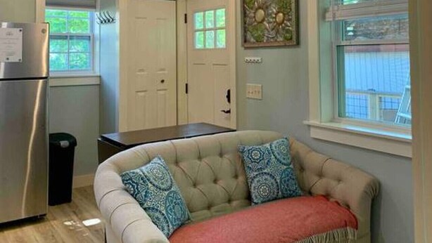 A cozy living room with a beige sofa, patterned cushions, a red throw, and a blue pendant light. - Sea Glass Cottage- New, Peaceful, Path to Beach (Bar Harbor)
