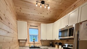 Una cucina compatta con pareti in legno, un frigorifero in acciaio inossidabile, un forno a microonde, un forno e un lavello.