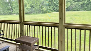 A covered outdoor deck with a view of a grassy field and trees. - Hadley Point Cottage #1 at Explore Acadia Cottages (Bar Harbor)