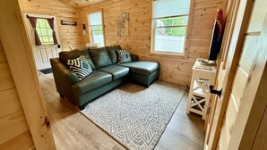 A wooden cabin interior with a sectional sofa, a patterned rug, and a small white table. - Hadley Point Cottage #1 at Explore Acadia Cottages (Bar Harbor)