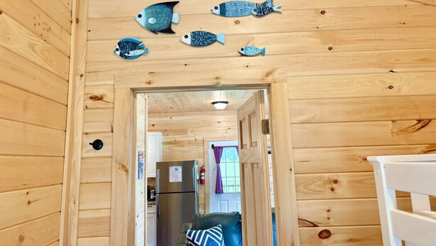 A wooden interior with a kitchen area, a refrigerator, and a door leading to another room. - Hadley Point Cottage #1 at Explore Acadia Cottages (Bar Harbor)