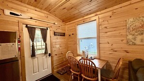 A cabin interior with a wooden interior, a dining table with chairs, a window, and a map on the wall.
