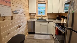 A compact kitchen with wooden walls, a sink, a refrigerator, and a window with a view.