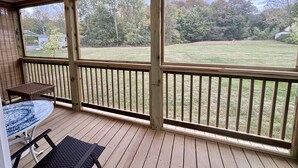 A covered porch with a table and chairs, a view of a grassy yard, and a wooden railing.