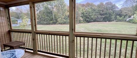 A covered porch with a table and chairs, a view of a grassy yard, and a wooden railing.