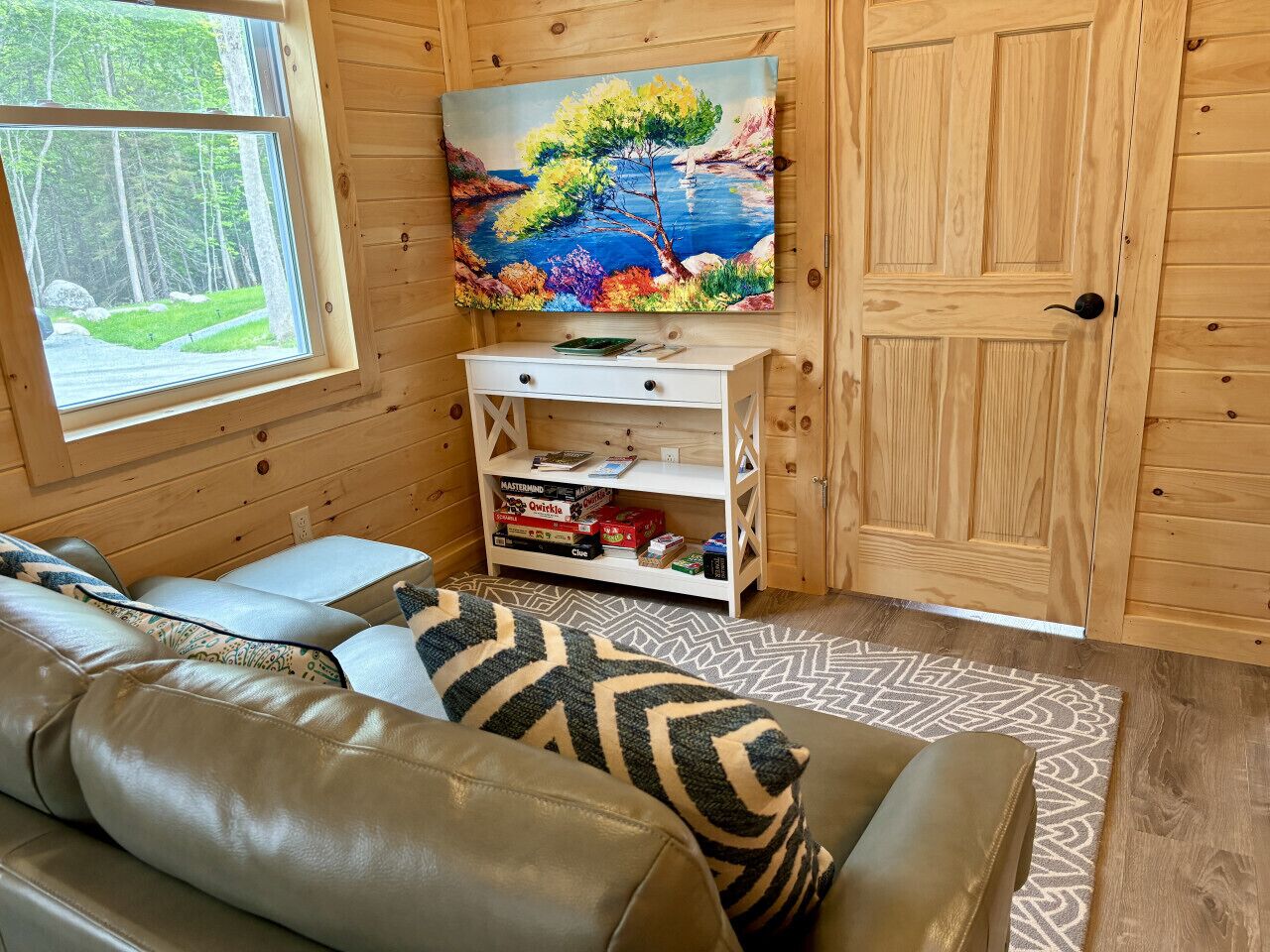 A cozy cabin interior with a sofa, a painting of a landscape, and a shelf with board games.