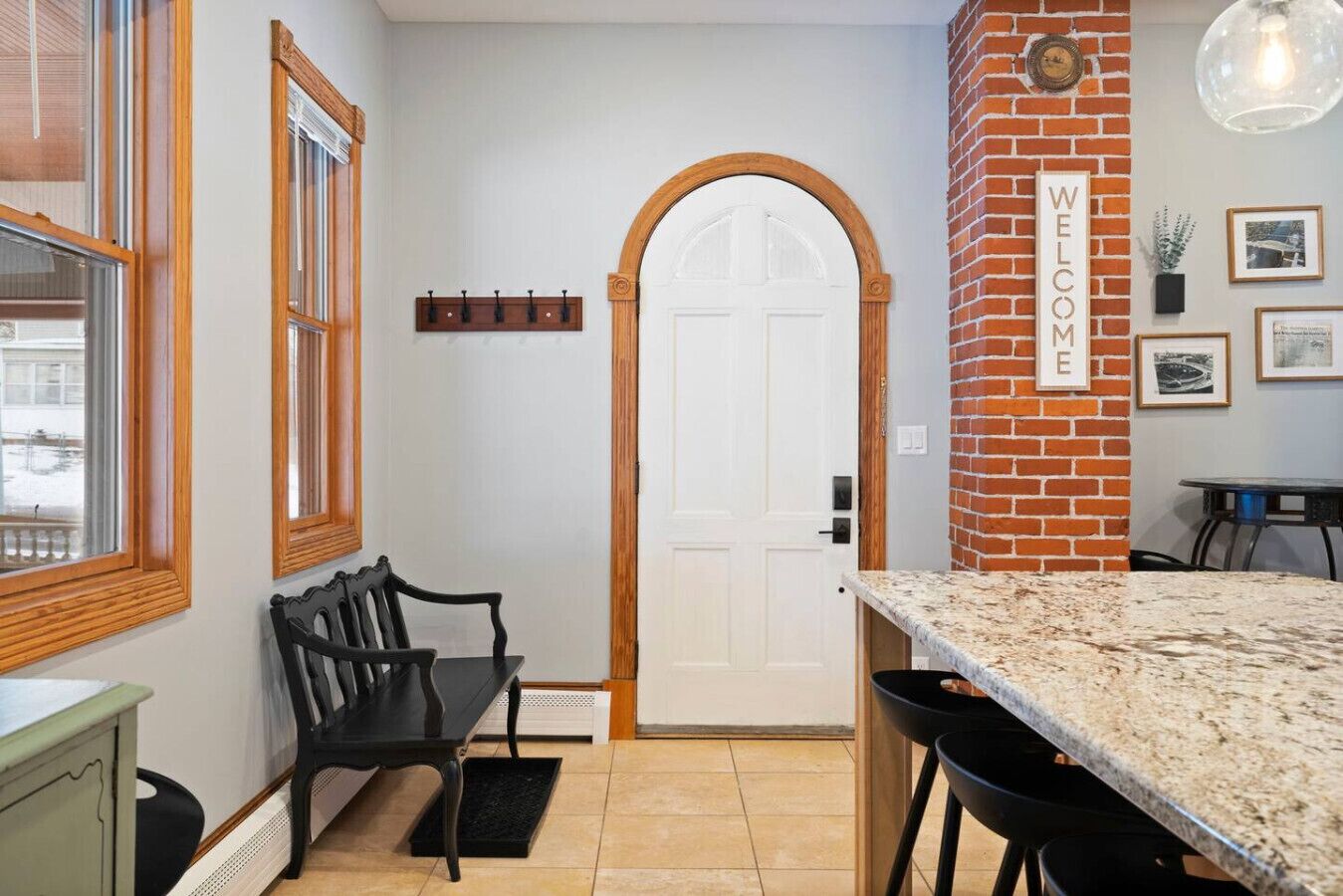 Una cocina con encimera de granito, un banco negro, una puerta blanca y una pared de ladrillo con un letrero que dice 'WELCOME'.