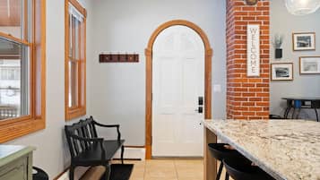 Una cocina con encimera de granito, un banco negro, una puerta blanca y una pared de ladrillo con un letrero que dice 'WELCOME'.