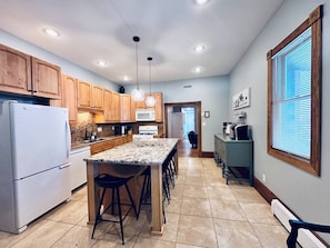 A kitchen with wooden cabinets, a white refrigerator, a granite countertop, and a bar stool.