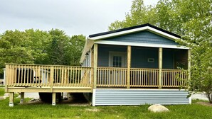 A small, single-story cabin with a wooden deck and a covered porch. - Sea Star Cottage #6 at Explore Acadia Cottages (Bar Harbor)
