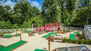 Een golfbaan met meerdere groene velden, een rode en witte speelconstructie en een witte omheining rondom het gebied.