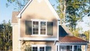 Een tweelaags huis met een veranda en een kleine aangebouwde garage.
