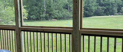 A wooden deck with a view of a grassy field and trees.