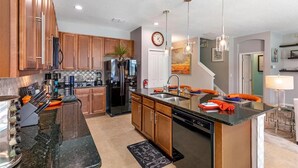 A modern kitchen with wooden cabinets, a black refrigerator, stainless steel appliances, and a central island with a sink. - 588 - Great Family Home near Disney, private pool - Bellavida Resort (Kissimmee)