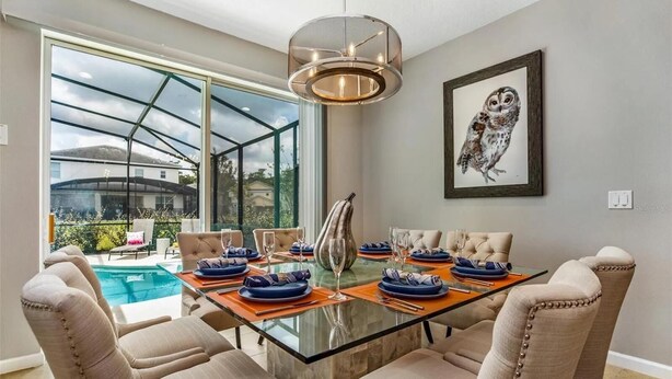 A dining area with a glass table, beige upholstered chairs, and a view of a swimming pool. - 588 - Great Family Home near Disney, private pool - Bellavida Resort (Kissimmee)