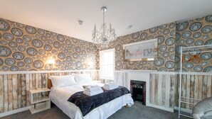 A bedroom with a bed, a chandelier, a fireplace, and patterned wallpaper. - The Bosun's Chair (Lymington)