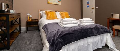 A neatly arranged hotel room with a bed, a nightstand, a desk, and a door with a sign.