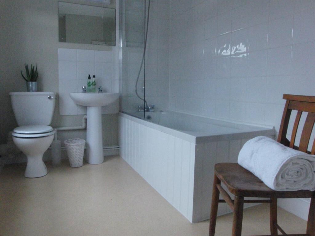 A bathroom with a toilet, sink, bathtub, and a chair with a towel.