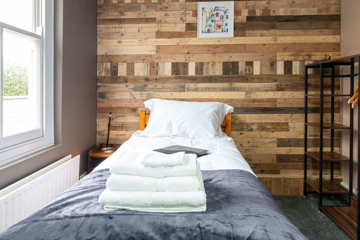 A bedroom with a wooden wall panel, a bed with white bedding, a bedside table with a lamp, and a radiator.