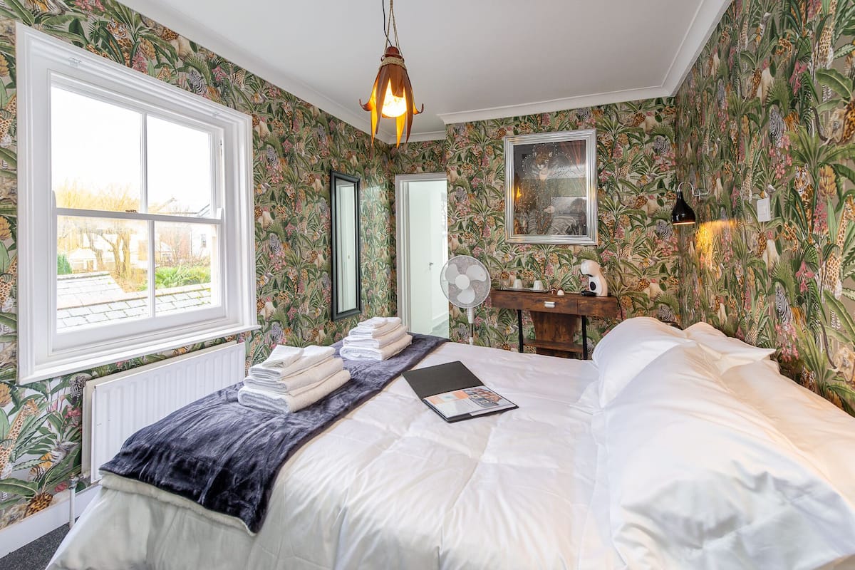 A bedroom with a large bed, a window, a fan, and a dresser.