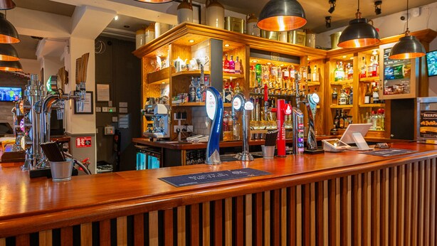 A bar area with multiple beer taps, a cash register, and shelves stocked with bottles. - The Bosun's Chair (Lymington)