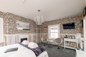 A hotel room with a patterned wallpaper, a chandelier, a bed with a laptop, two chairs, a small table, and a TV mounted on the wall. - The Bosun's Chair (Lymington)