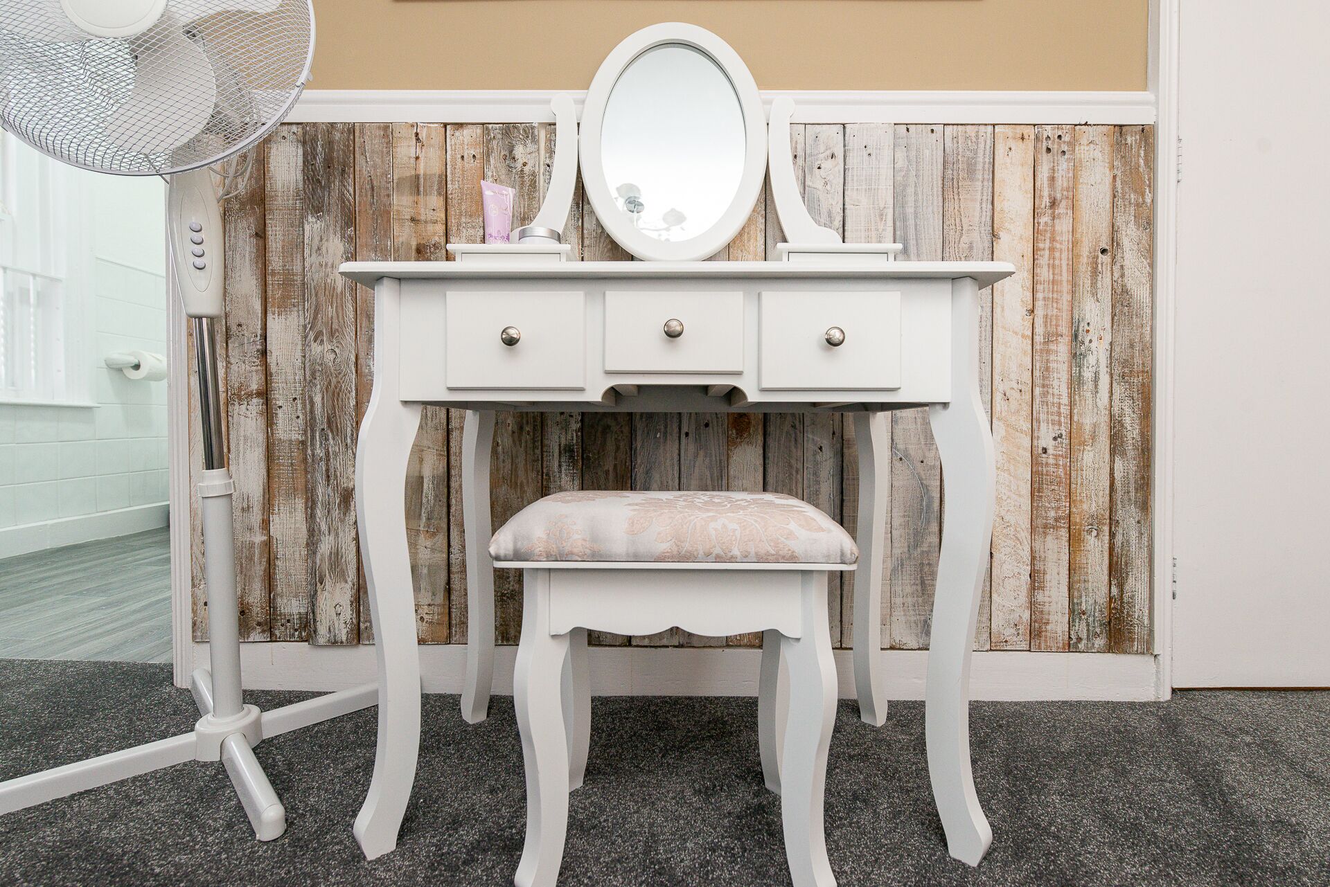 A white vanity with a mirror and a bench, set against a rustic wooden backdrop.