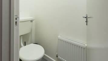 Ein kleines, weißes Badezimmer mit Toilette, einem weißen Heizkörper und einem grauen Holzboden.
