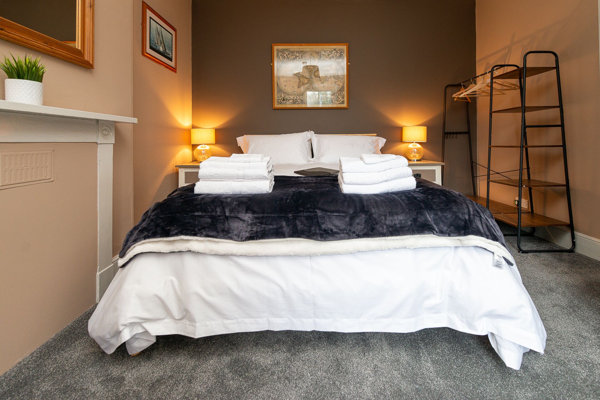 A neatly made bed with white and black bedding, two bedside lamps, a framed map on the wall, and a small plant on the nightstand.