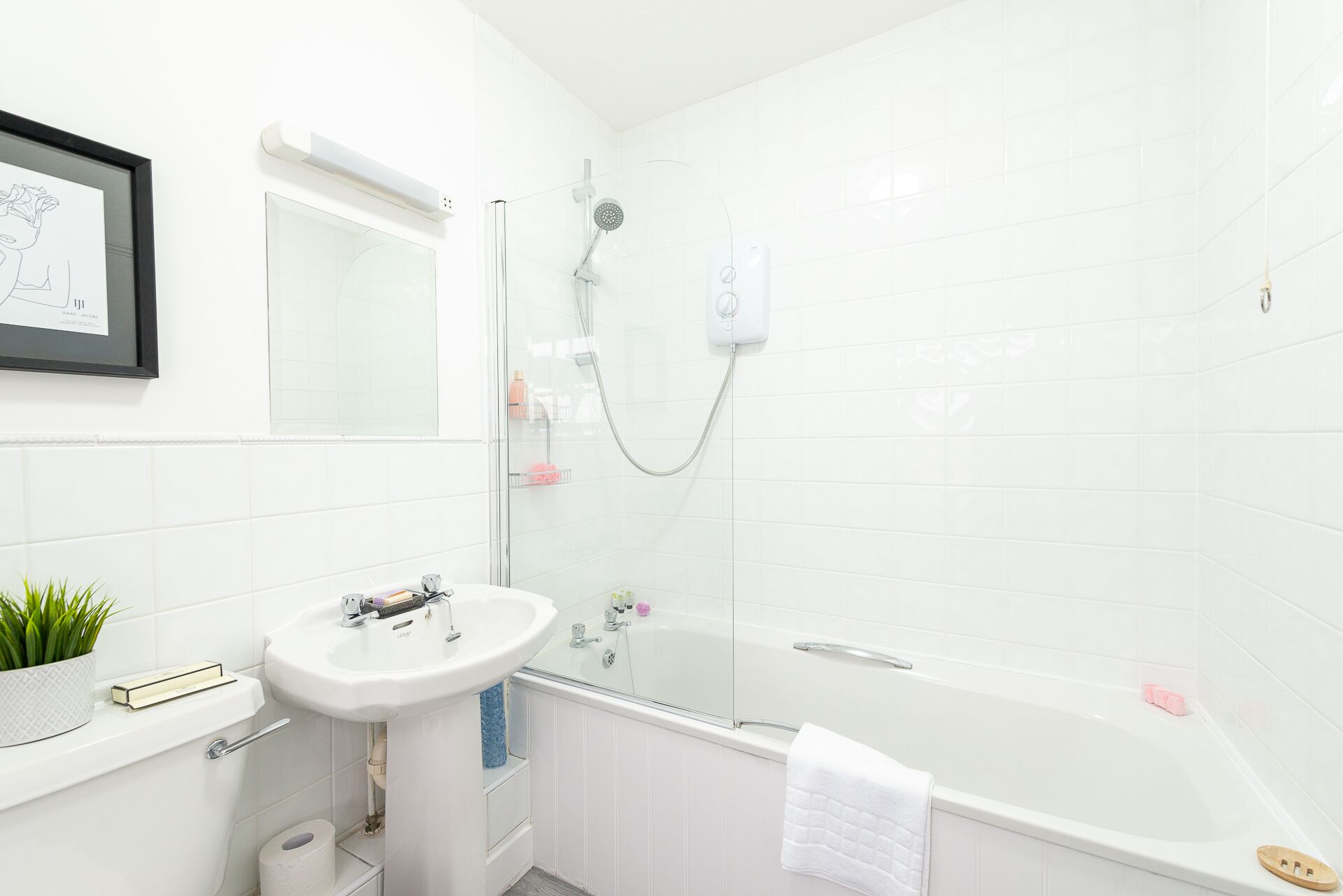 Une salle de bain moderne avec un lavabo, des toilettes et une baignoire, tous de couleur blanche. Un tableau encadré est accroché au mur et une plante en pot est posée sur le comptoir.