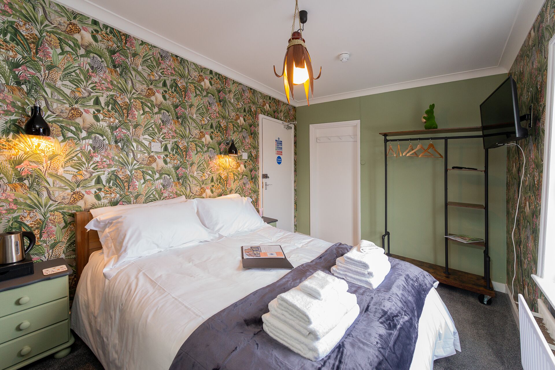 A hotel room with a bed, a nightstand, a lamp, a wardrobe, and a mirror.
