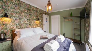 A hotel room with a bed, a nightstand, a lamp, a wardrobe, and a mirror.
