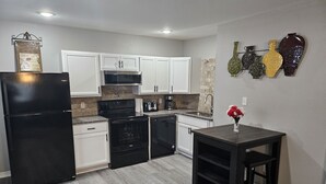Una cocina moderna con armarios blancos, un refrigerador negro, estufa y lavavajillas. Hay una pequeña mesa con un jarrón de flores.