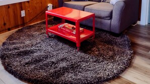 Ein gemütliches Wohnzimmer mit einem grauen Sofa, einem roten Couchtisch und einem großen Fenster.